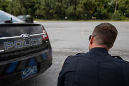 Officer behind cruiser with weapon drawn.